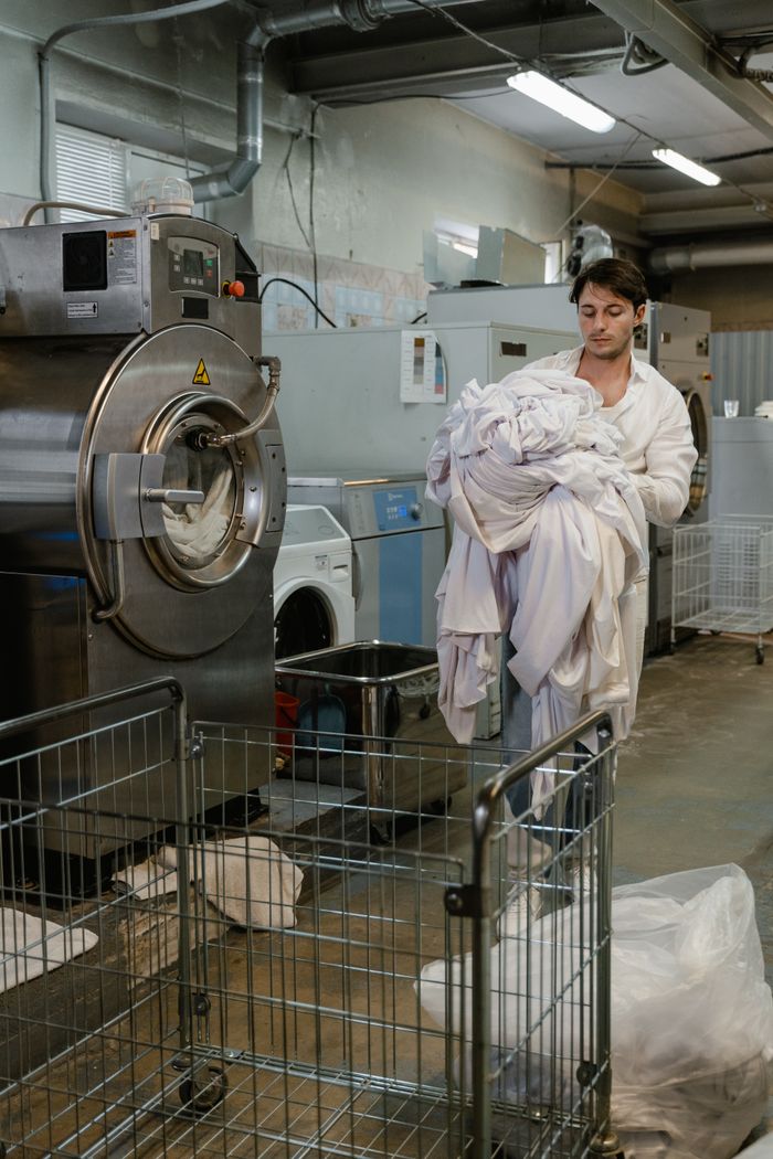 A man carries a large load of laundry in a commercial laundry facility.